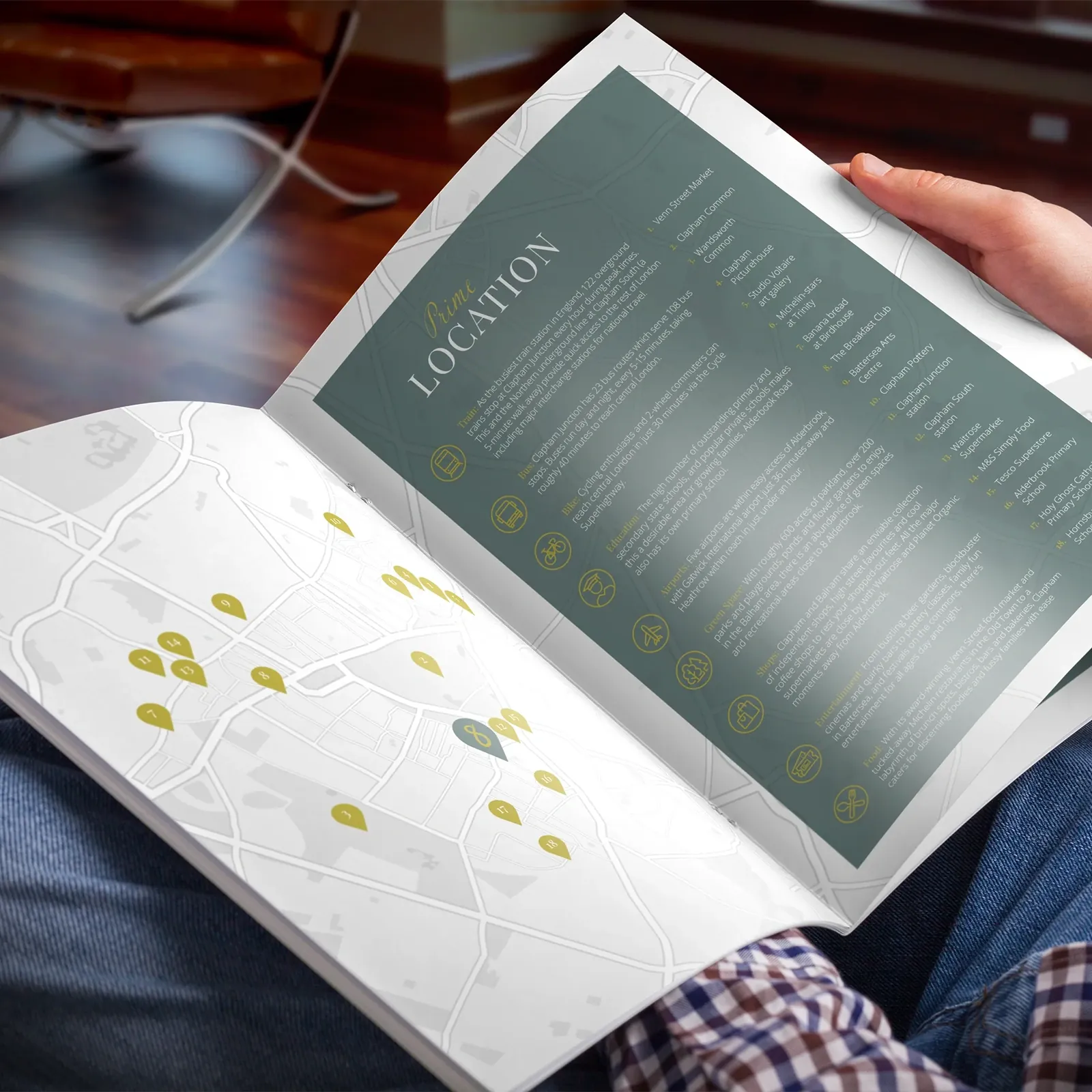 Reader holding the 8 Alderbrook brochure open at the Prime Location spread, with a map of Clapham dotted with numbered gold pins