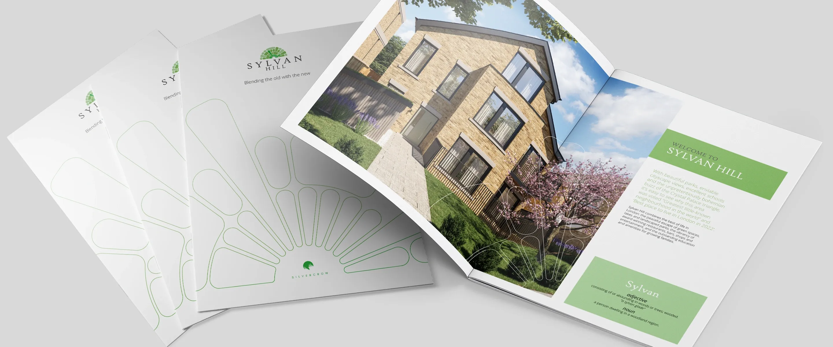 Sylvan Hill brochure covers beside a copy open at a CGI of the stone-fronted houses and the green Sylvan Hill introduction panel