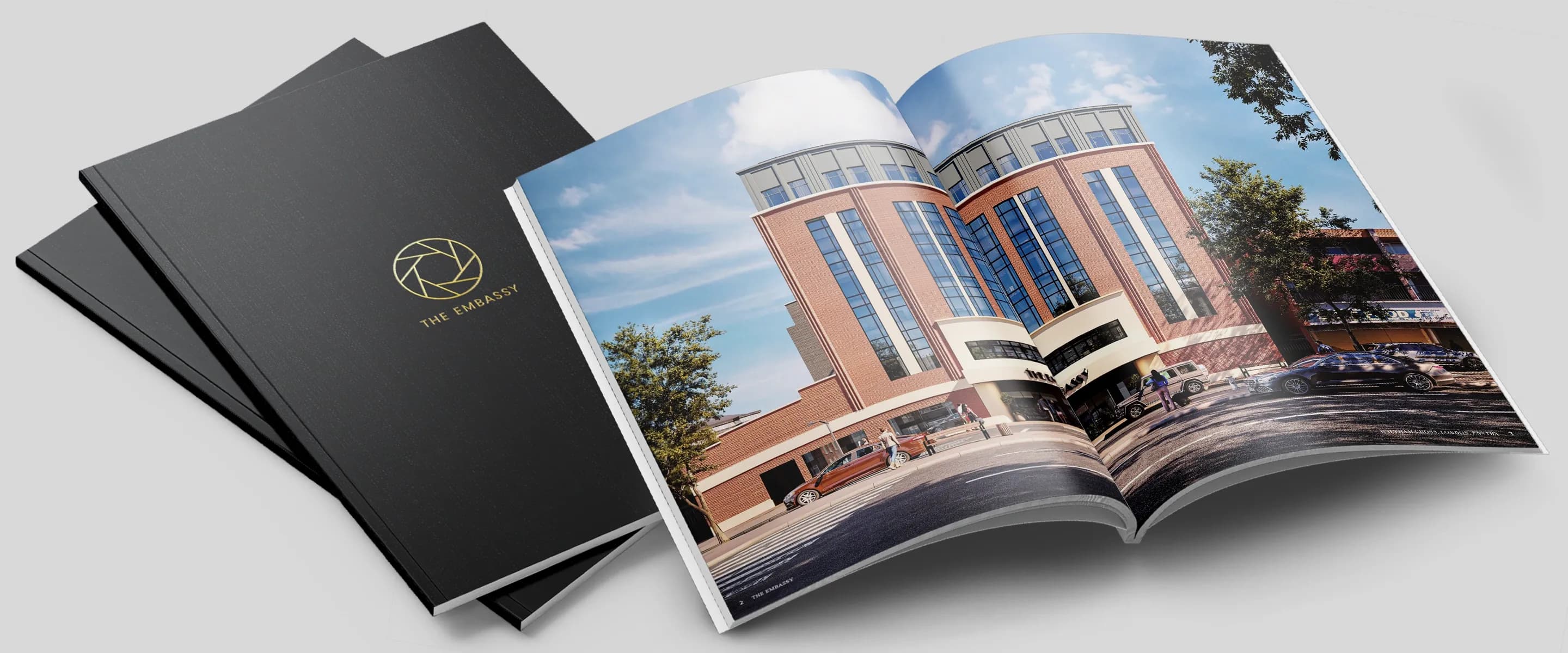 The Embassy brochure's black covers with the gold logo beside a copy open at a CGI of the red-brick building